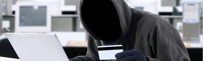 Vol sur Internet - un homme portant une cagoule et tenant une carte de crédit, assis derrière un ordinateur portable.