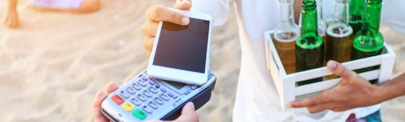 Jeune homme utilisant un téléphone intelligent pour le paiement sans contact sur la plage. 