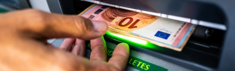 Gros plan de la main d'une personne retirant des euros d'un distributeur automatique de billets.