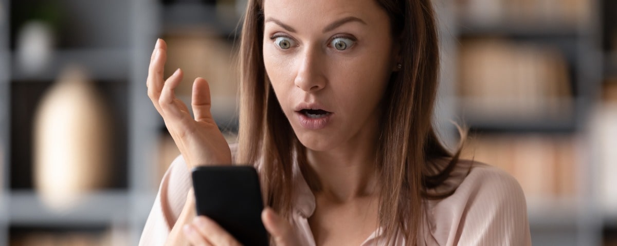 Plan rapproché d'une jeune femme choquée regardant l'écran de son téléphone portable, ayant reçu une notification de dette bancaire. 