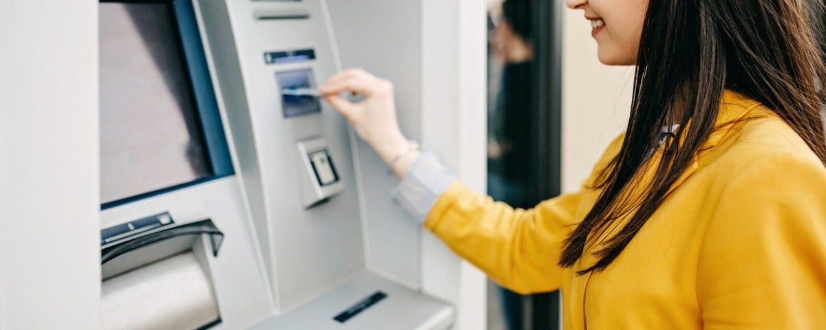 Une jeune jolie femme insérant sa carte bancaire sur le guichet automatique pour tirer des billets.