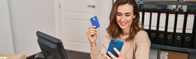 Jeune femme travaillant dans le commerce électronique, utilisant un smartphone et une carte de crédit au bureau.