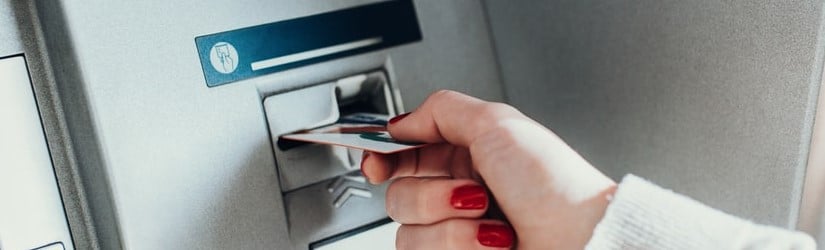 Main d’une personne insérant une carte de crédit dans le distributeur automatique de billets pour retirer de l'argent.