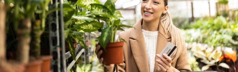 Jeune femme dans une jardinerie achetant des plantes avec une carte de crédit.