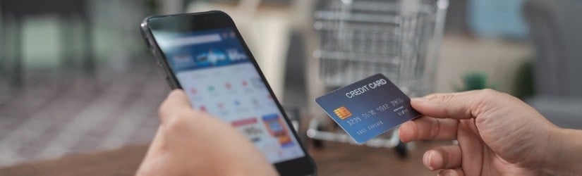 Jeune homme tenant dans ses mains un téléphone mobile intelligent montrant le succès du paiement à l'écran et une carte de crédit sur une table.