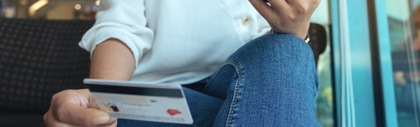 Image en gros plan d'une femme assise dans un café, tenant une carte de crédit et utilisant des services bancaires mobiles.