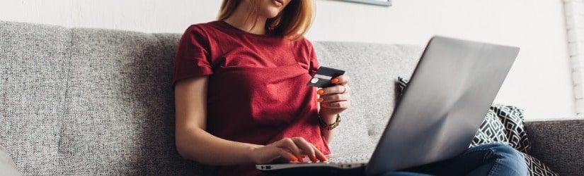 Femme faisant des achats en ligne avec un ordinateur portable et une carte de crédit à la maison.
