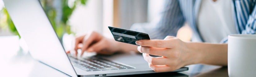 Gros plan sur une jeune femme qui gère ses opérations bancaires en ligne avec son ordinateur portable et sa carte de crédit à la maison. 