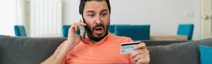 Un homme stressé tient une carte bancaire et parle au téléphone.