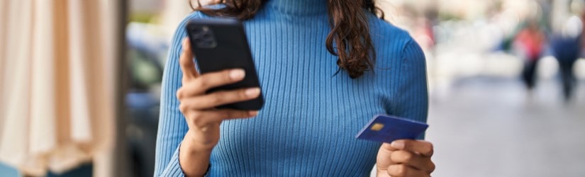 Jeune femme afro-américaine utilisant un smartphone et une carte de crédit dans la rue