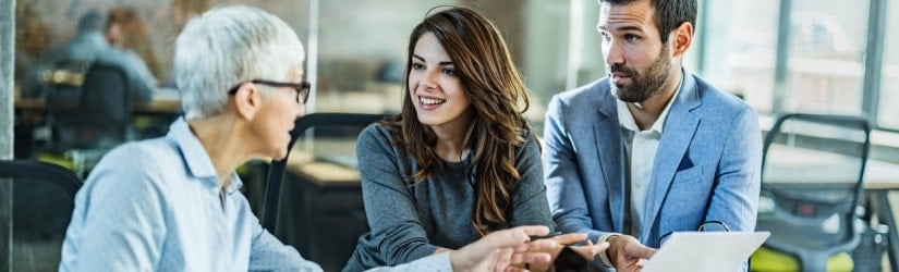 Agent financier d'assurance senior s'entretenant avec un jeune couple au sujet de la paperasserie lors d'une réunion au bureau.