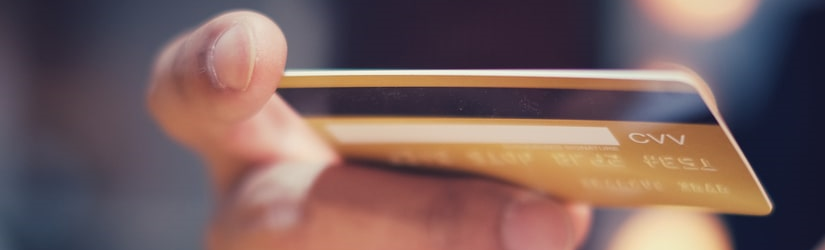 Un jeune homme d'affaires souriant utilise une carte de crédit et un ordinateur portable dans un bureau moderne.