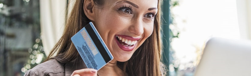 Femme souriante avec carte de crédit et ordinateur portable.