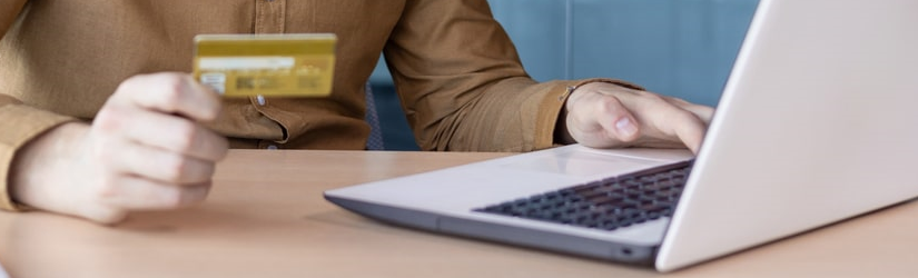 Un jeune homme d'affaires sérieux travaille au bureau sur un ordinateur portable et effectue des transactions avec une carte de crédit dans la main.