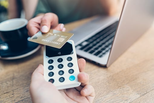 Paiement sans contact avec une carte bancaire sur un terminal portable, avec un ordinateur portable en arrière-plan