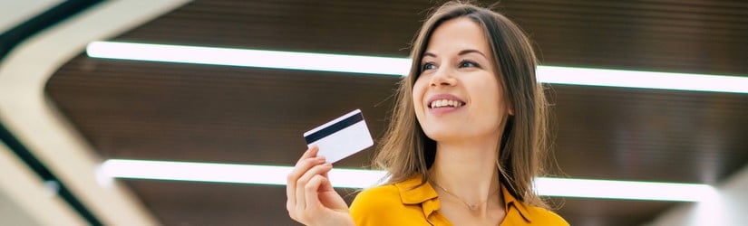 Une jeune femme souriante et ravissante pose avec une carte de crédit et des sacs de courses dans un centre commercial.