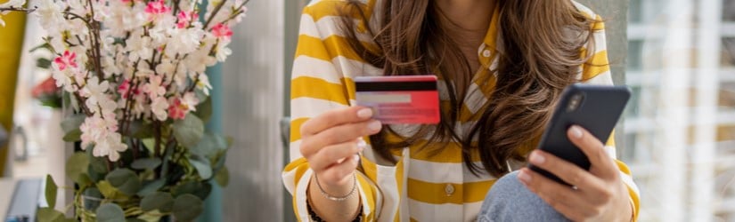 Une jolie femme tenant sa crédit carte et son smartphone pour faire un achat en ligne.