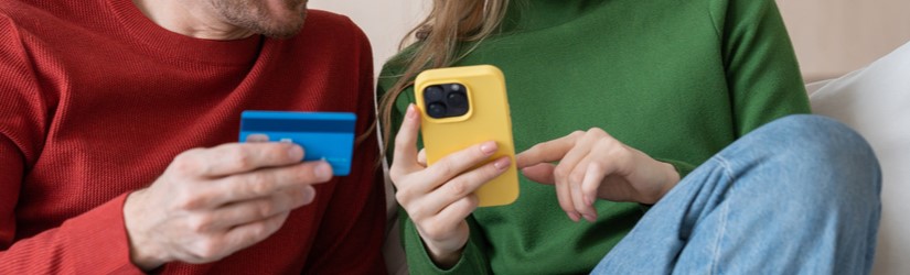 Couple souriant assis sur un canapé avec un téléphone portable et une carte de crédit, dépensant de l'argent dans des boutiques en ligne.