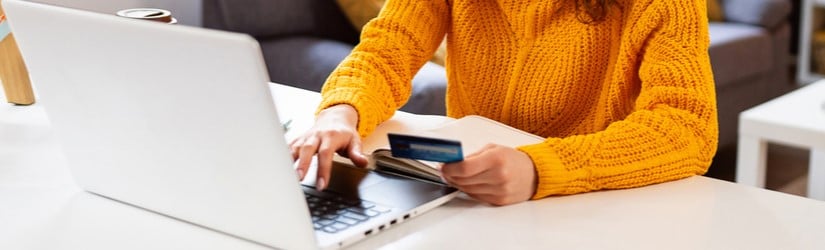 Jeune femme caucasienne tapant les informations d'une carte de crédit lors d'un achat en ligne depuis son bureau à domicile, pendant une pause de travail.