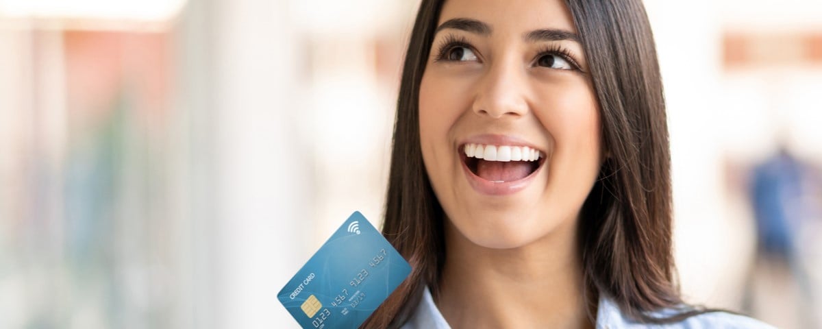 Une jeune femme enthousiaste regarde au loin en rêvassant tout en tenant sa carte de débit et ses sacs à provisions.