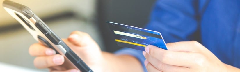 Une femme tient dans sa main un téléphone portable et une carte de crédit avec affichage de la page des détails de paiement. 